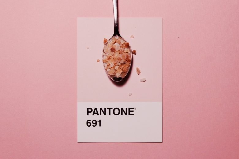 Spoon with coarse pink salt placed over a Pantone 691 color swatch on a pink background