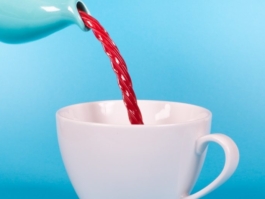 Red liquid being poured into a white cup against a blue background