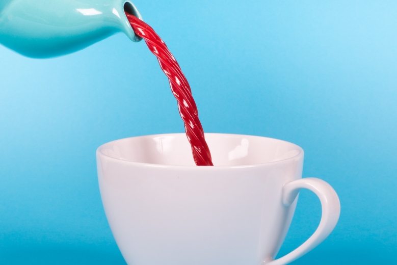Red liquid being poured into a white cup against a blue background