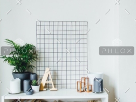 Minimalist white shelf with decorative plants, candles, and wooden letter A against a white wall with a black grid decor