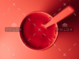 Top view of a red smoothie or drink in a glass with a spoon inside against a red background