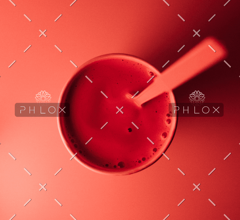 Top view of a red smoothie or drink in a glass with a spoon inside against a red background