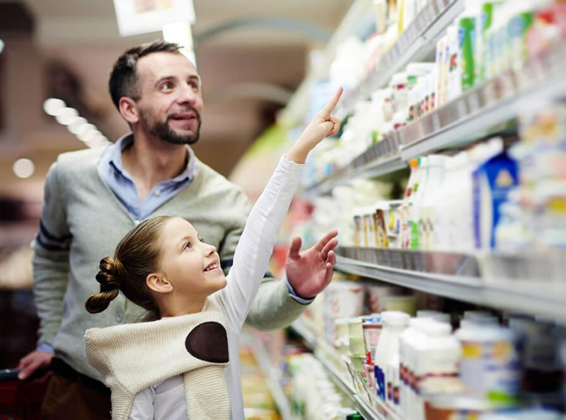 Father and daughter shopping together in a grocery store aisle filled with various packaged products