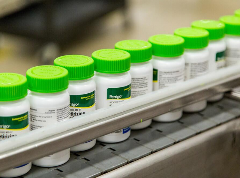 Bottles of cetirizine medication with green caps on a manufacturing line at Perrigo pharmaceutical manufacturer