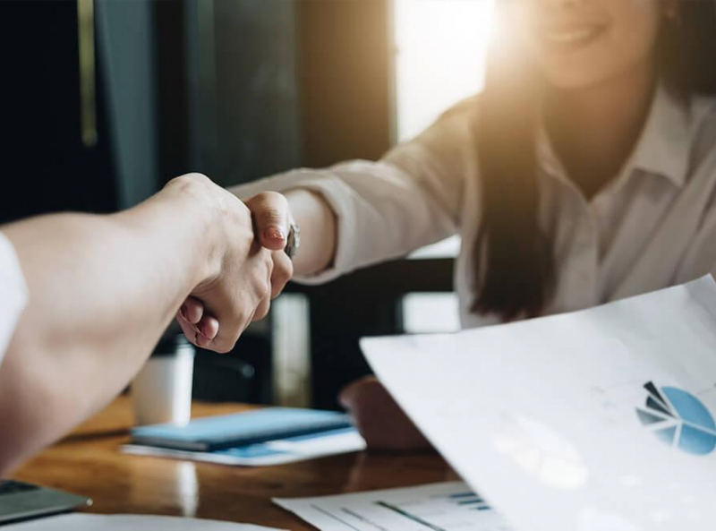 Close-up of a business handshake over a desk with financial documents and a laptop in a professional setting