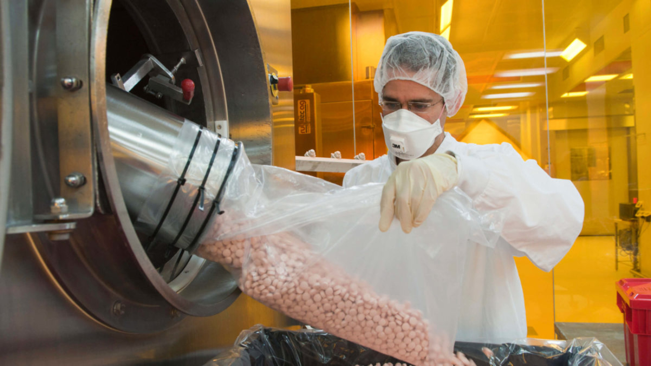 Pharmaceutical worker in protective gear handling tablet capsules in manufacturing facility