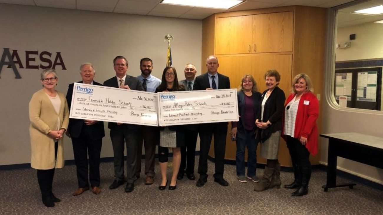 Group of people holding oversized Perrigo Foundation donation checks for community schools in a formal indoor setting