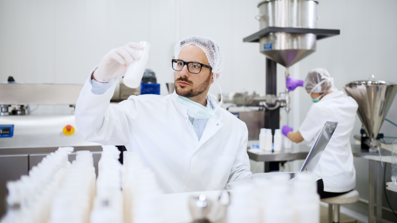 Pharmaceutical worker inspecting white plastic bottles in GMP manufacturing facility