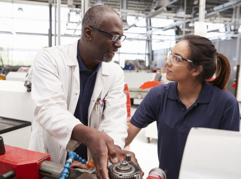 Experienced technician mentoring female apprentice in advanced manufacturing facility