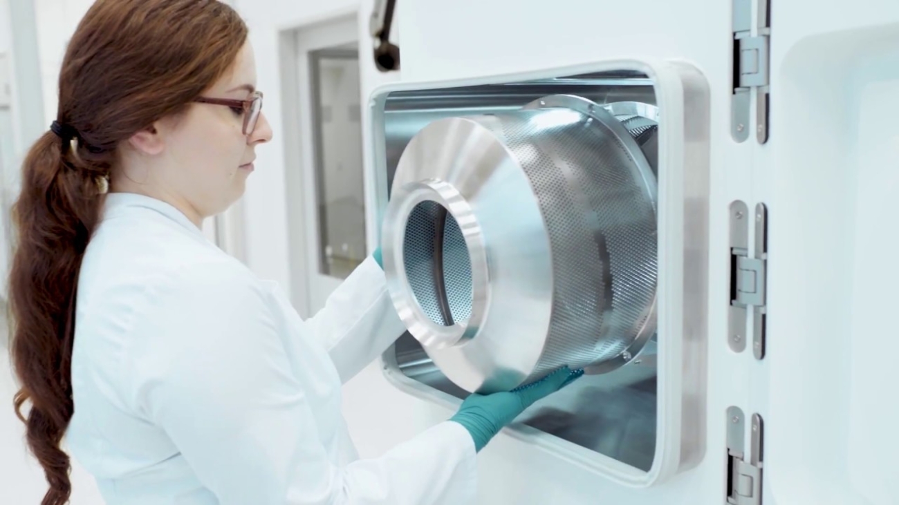 Lab technician inserting metal cylinder into industrial sterilizer in pharmaceutical manufacturing facility