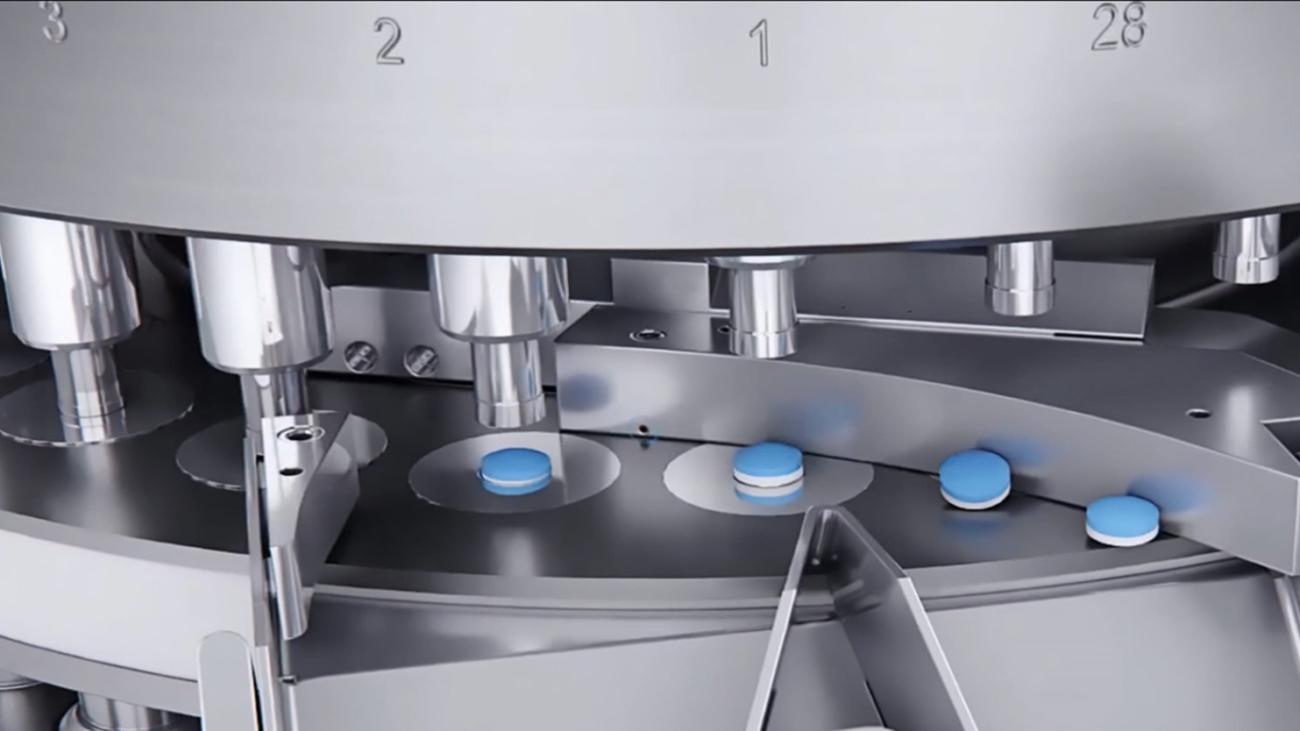 Close-up of blue and white tablets on a stainless steel pharmaceutical tablet press machine in production