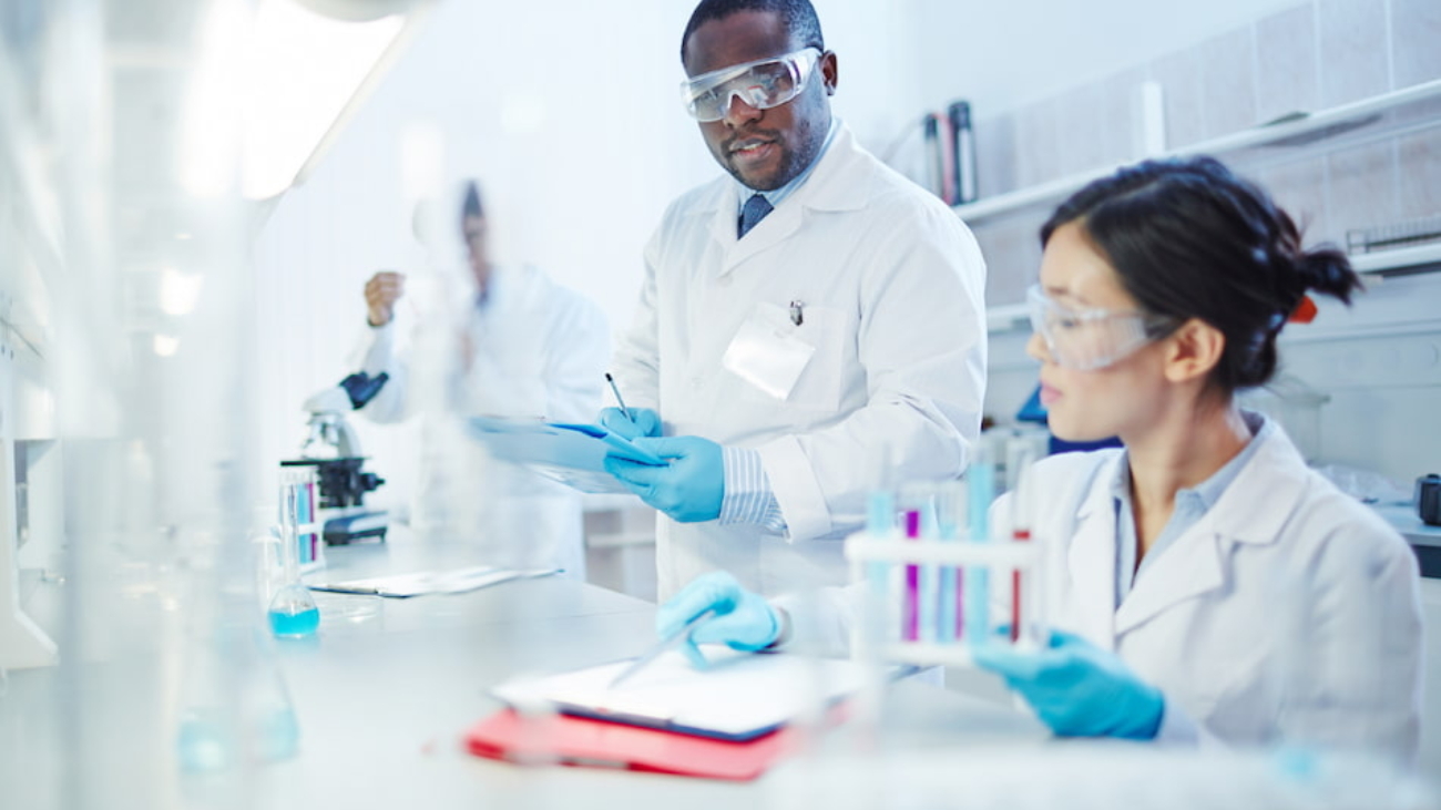 Scientists in a laboratory wearing lab coats and protective eyewear, conducting experiments with test tubes and recording observations