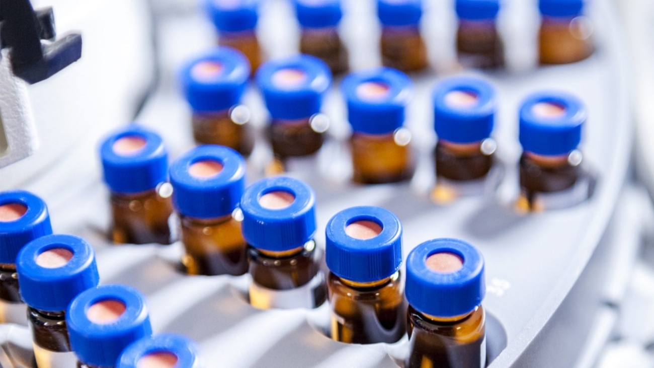 Close-up of multiple small brown glass vials with blue caps arranged in a laboratory rack for peptide or pharmaceutical manufacturing