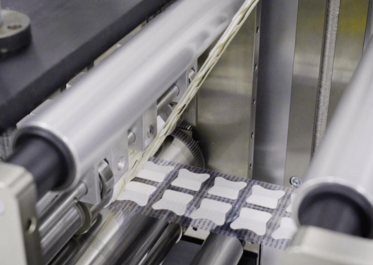 Automated packaging machine producing adhesive nicotine pouches