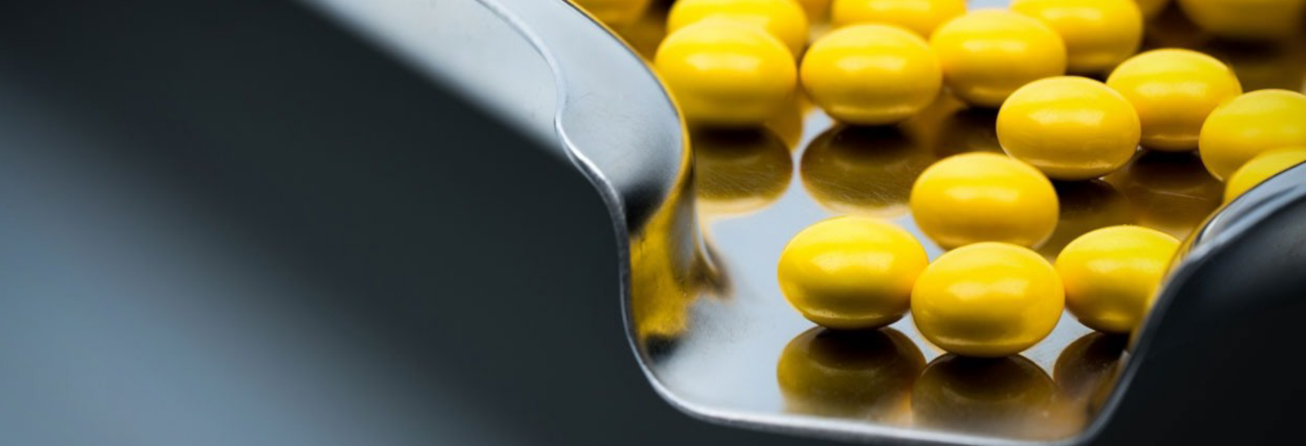Close-up of yellow pharmaceutical pills on a metal scoop reflecting their shape