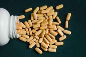 Close-up of beige peptide capsules spilled from white bottle on dark surface