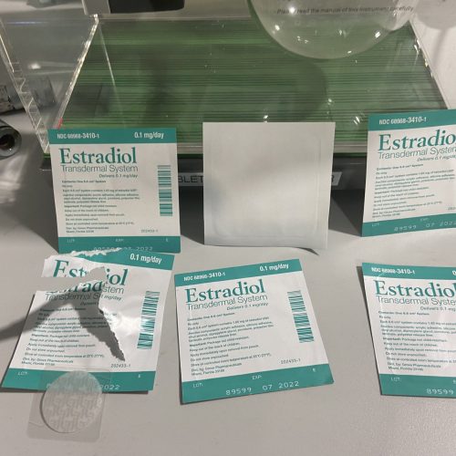Estradiol Transdermal System manufacturer packaging and patches arranged on a surface with one patch partially peeled